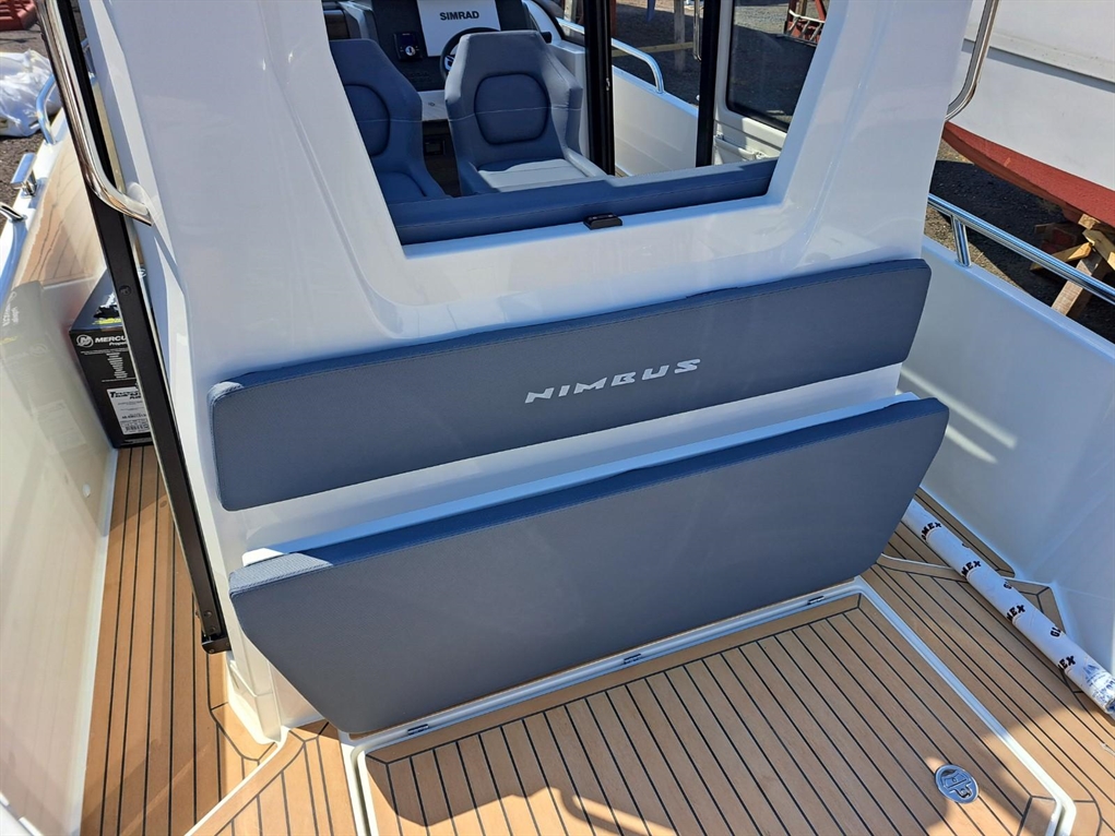 Interior view of a Nimbus boat showing blue cushioned seats, wooden flooring, and a SIMRAD dashboard.